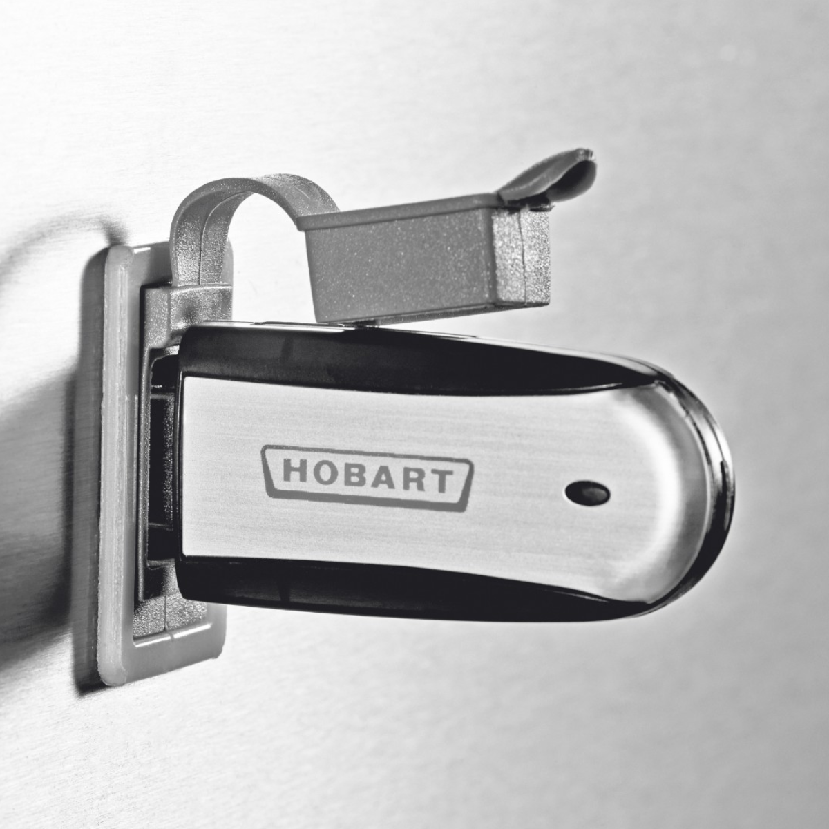 A close-up of a Hobart Profi AMXT Double Rack Passthrough Glass & Dishwasher | Dishwashers Direct power tool mounted on a wall, showing its brushed metal body, black accents, and the Hobart logo.